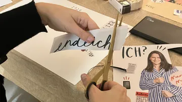 Hände schneiden Papier mit Schere in Bastelumgebung.