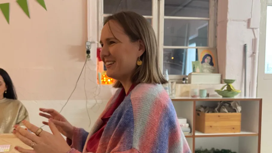 Woman smiling, gesturing, indoors at a table.