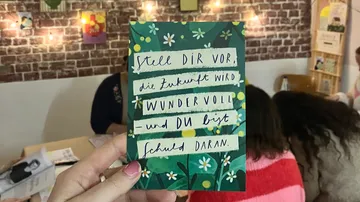 Hand holding card with German text, cozy room.