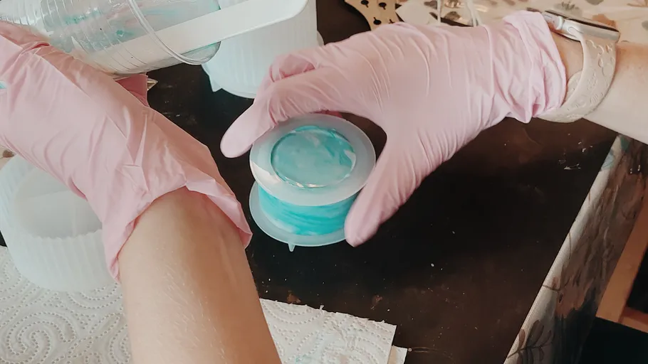 Hands wearing gloves mixing resin in molds.