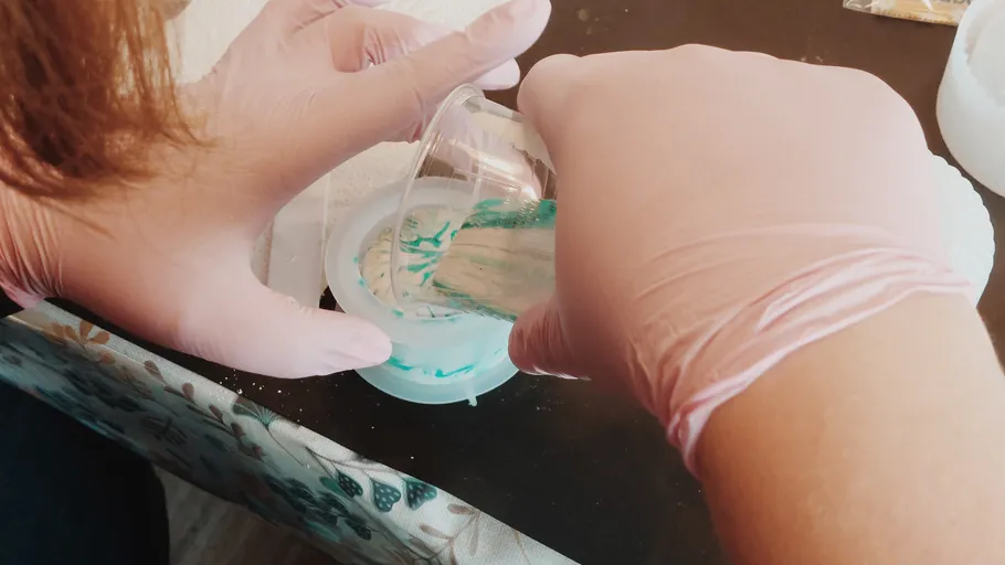 Hands pouring resin into mold on table.