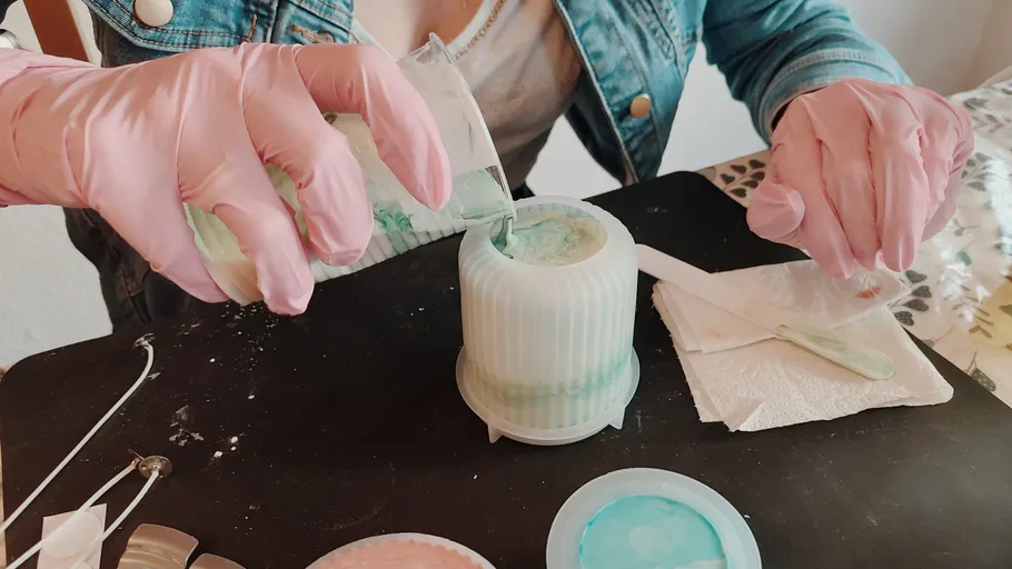 Person pouring green mixture into mold indoors.