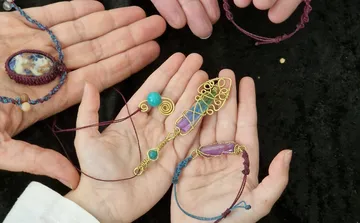 Hände halten handgefertigten Edelsteinschmuck auf schwarzem Stoff.