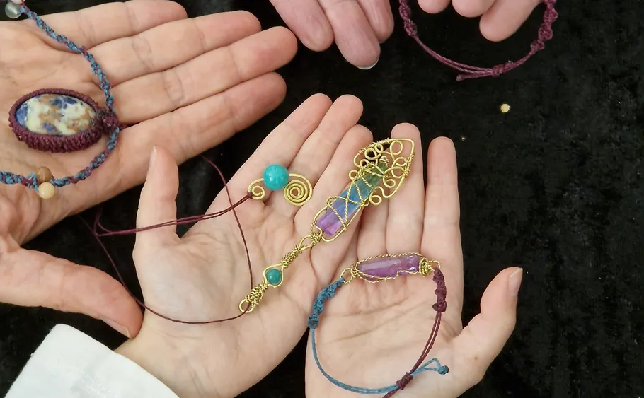 Hands holding handmade gemstone jewelry on black cloth.