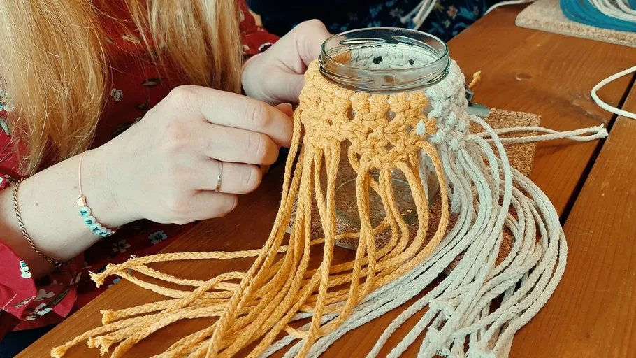 Woman crafting macramé on jar at table.