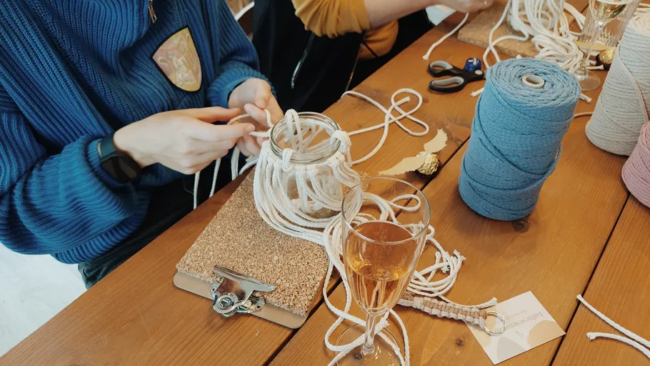 Person crafting macramé at wooden table.