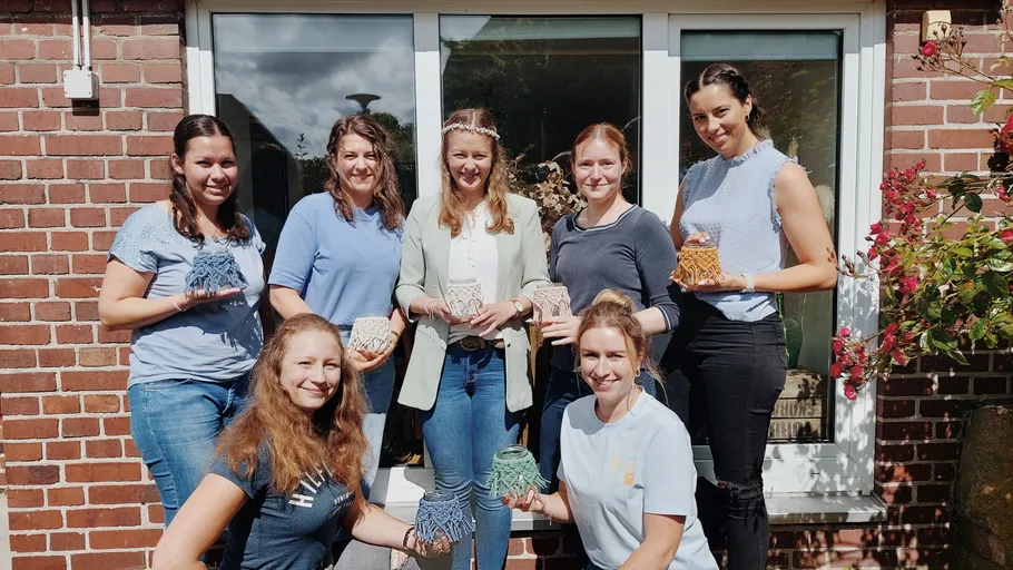Seven women holding crafted lanterns outside brick house.