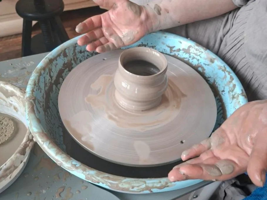 Hands shaping clay pot on pottery wheel.