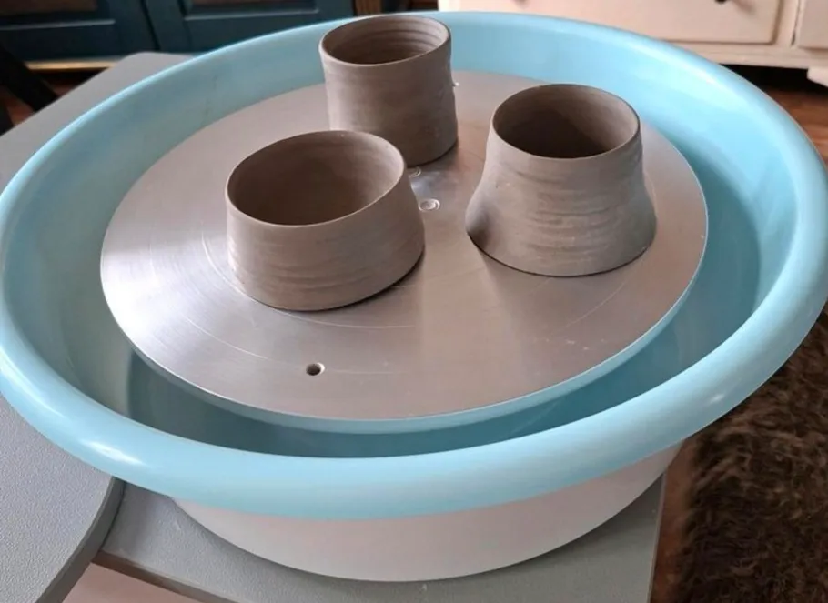 Three clay pots on a pottery wheel indoors.