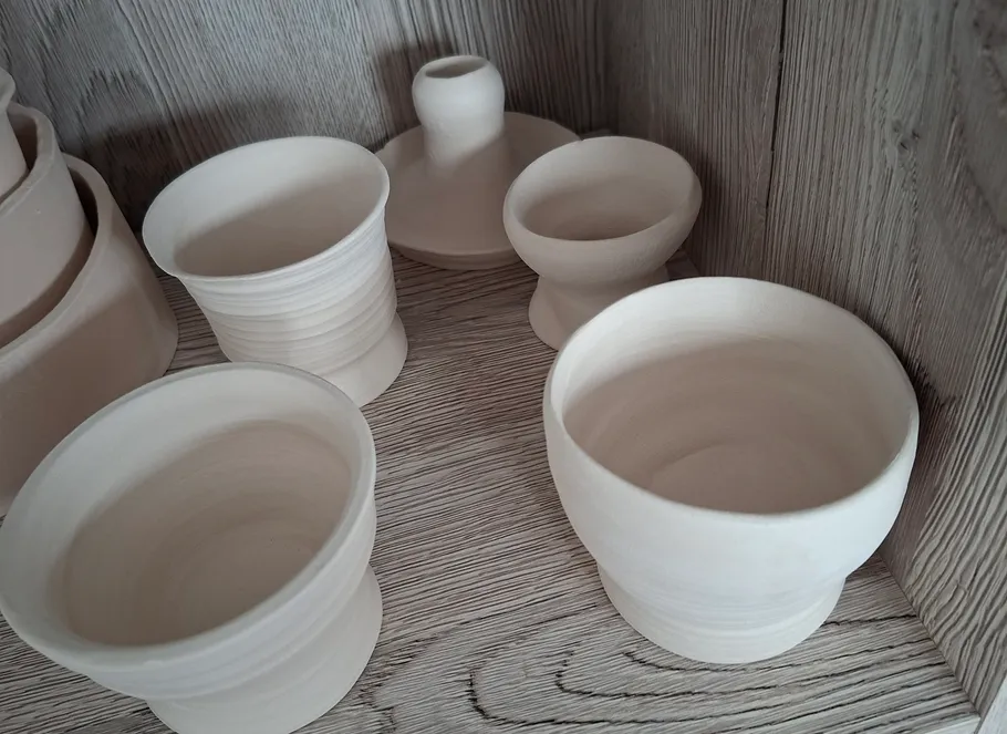 Weiße Tontöpfe auf Holztisch angeordnet.