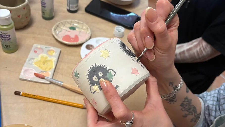 Hands painting a pottery piece at a table.