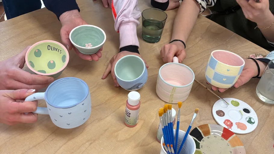 People holding painted ceramic cups and bowls.
