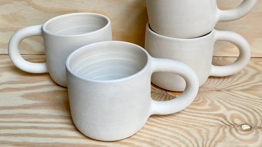 Four white ceramic mugs on wooden surface.