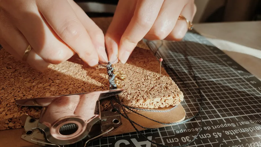 Hände knüpfen Armband auf Korkbrett.