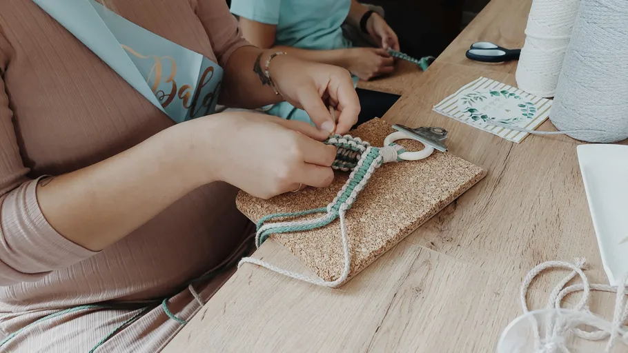 Person crafting macrame on wooden table.