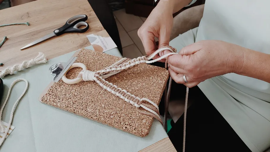 Person creating macramé on cork board indoors.