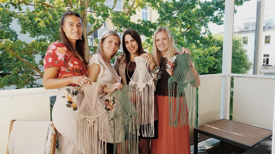 Vier Frauen halten Makramee-Kunst auf Balkon.