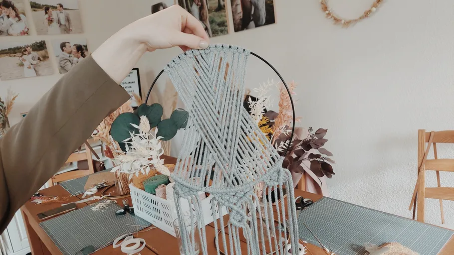 Hand holding macramé piece in decorated room.