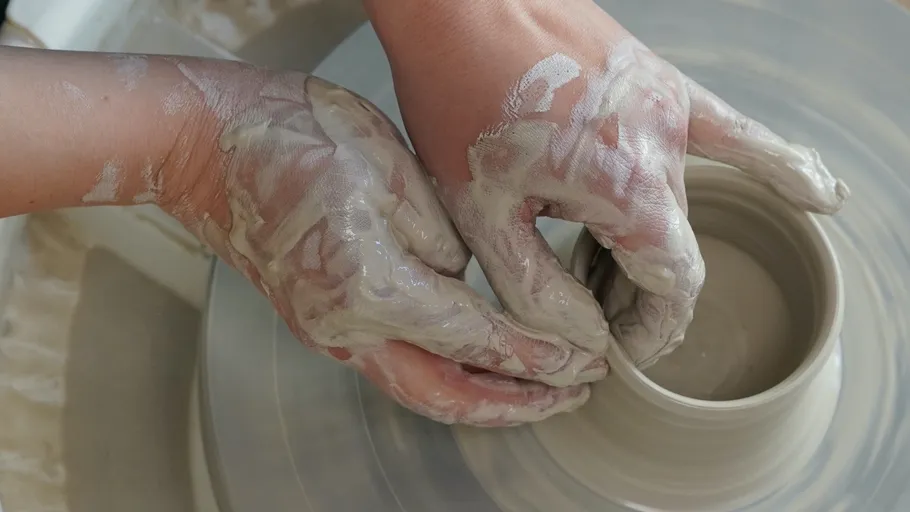 Hands shaping clay on a pottery wheel.