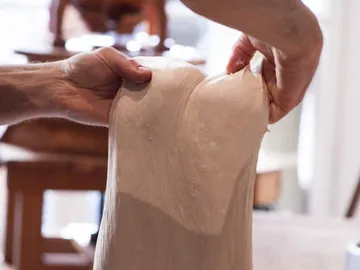 Dough is stretched by hands in a kitchen environment.