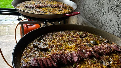 Two pans of paella cooking outdoors.