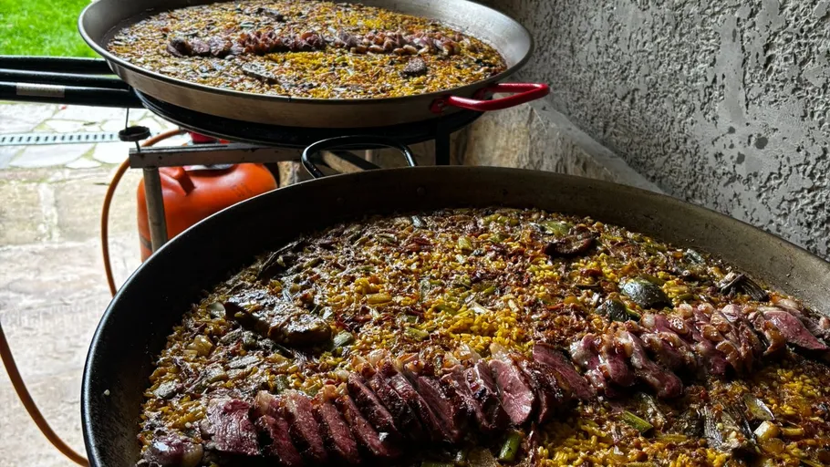 Two pans of paella cooking outdoors.