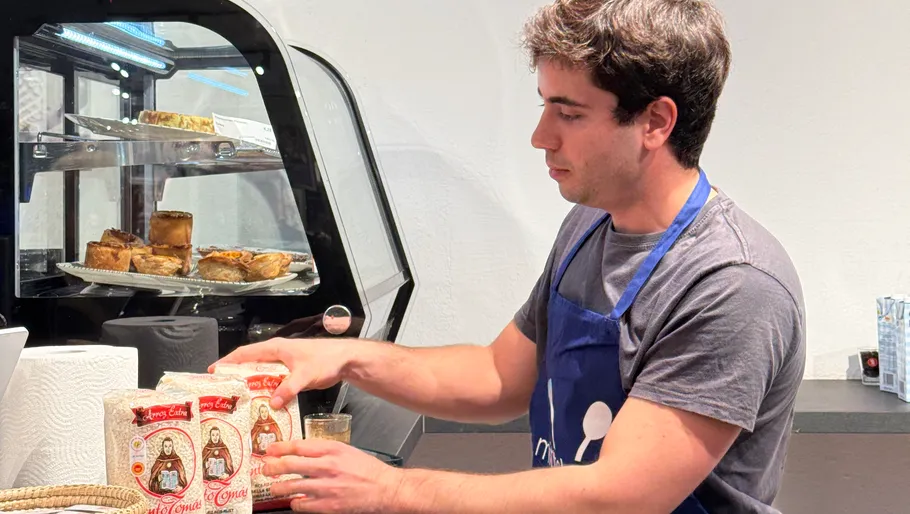 Mann ordnet Tüten auf Theke neben Gebäckvitrine.