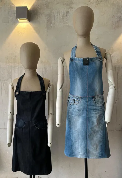 Zwei Schaufensterpuppen tragen Denim-Schürzen in beleuchtetem Raum.