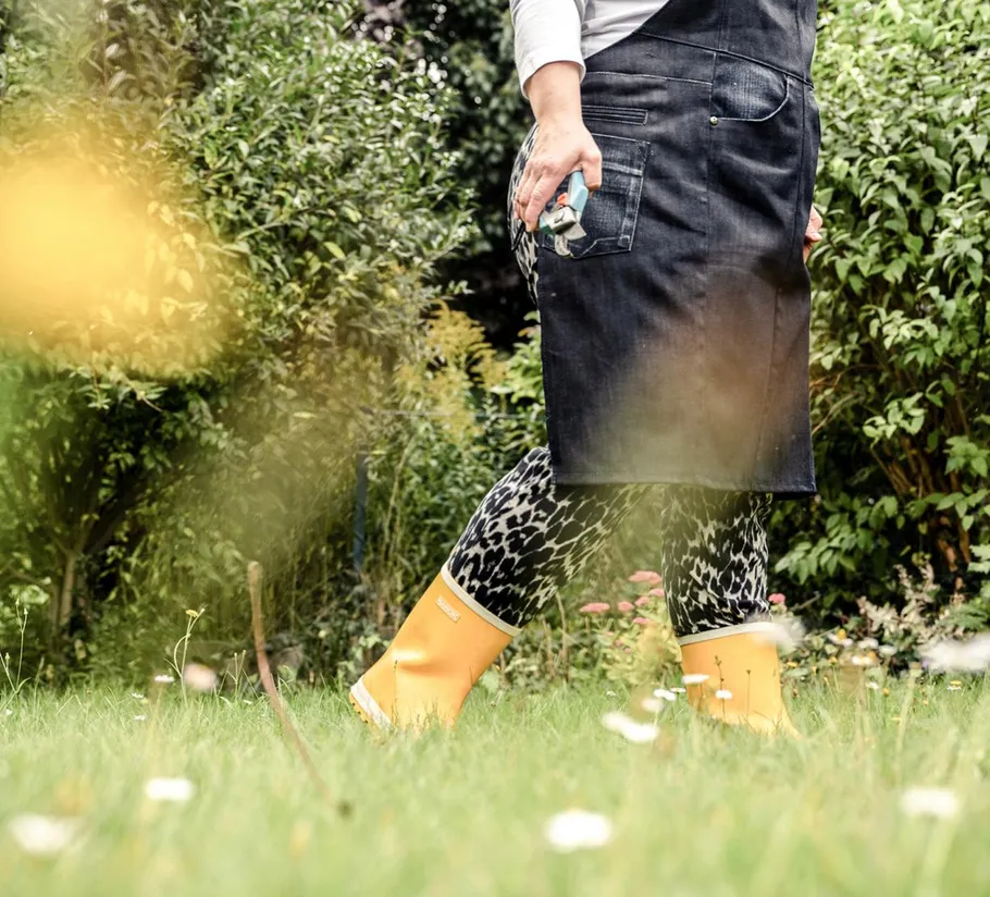 Person im Garten mit Gummistiefeln und Schürze.