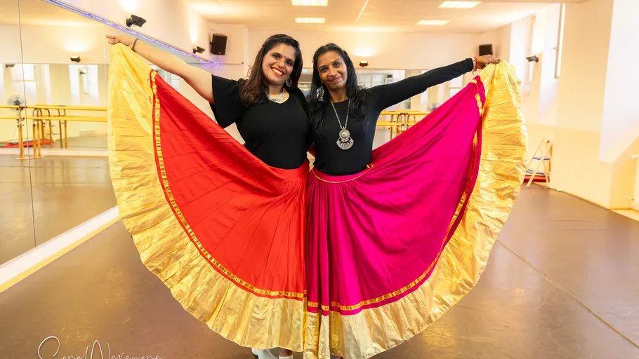 Two women pose in dance skirts in studio.