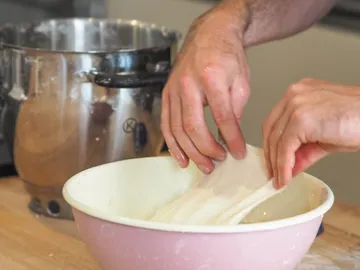 Hands pull dough out of a bowl in the kitchen.