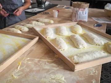 Dough pieces lie on wooden plates while someone prepares them.