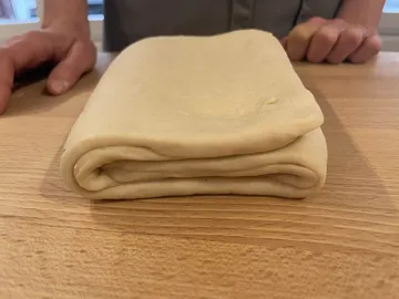 Folded dough is laid out on a wooden table.