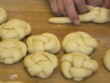 Teig wird zu geflochtenen Brötchen auf einer Holzoberfläche geformt.