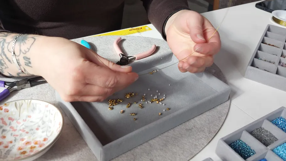Person stringing beads at craft table.