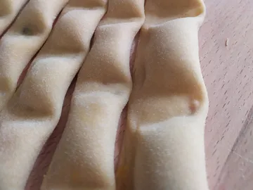 Strips of dough lie on a wooden surface, ready for processing.