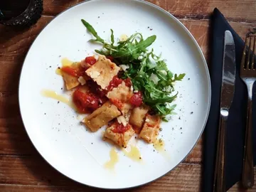 Pasta-Gericht mit Tomatensauce und Rucola auf weißem Teller.