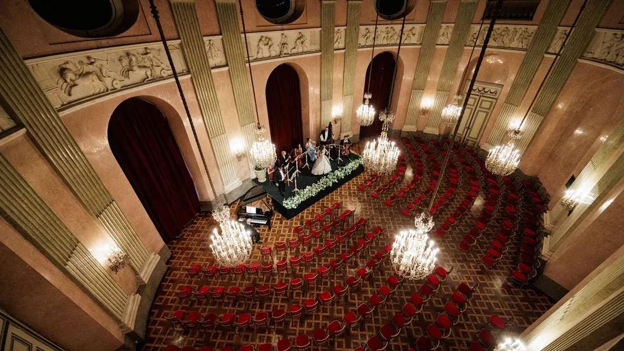 Orchester spielt in elegantem, leerem Konzertsaal.