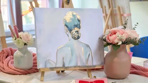 Painting of woman on easel with flowers nearby.