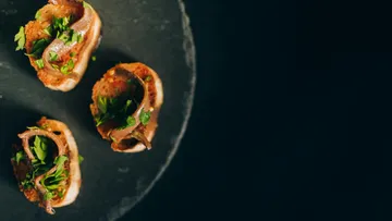 Three meat canapés with herbs on slate.