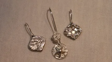 Three silver earrings on beige fabric.
