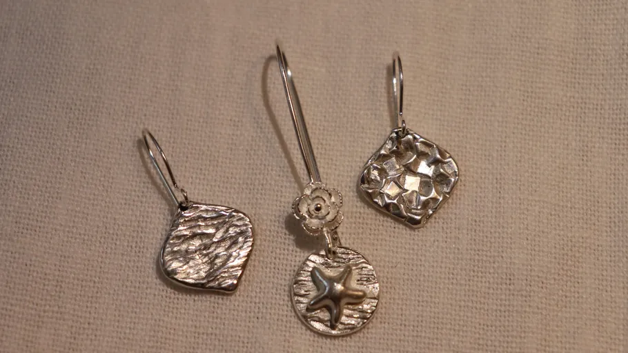 Three silver earrings on beige fabric.