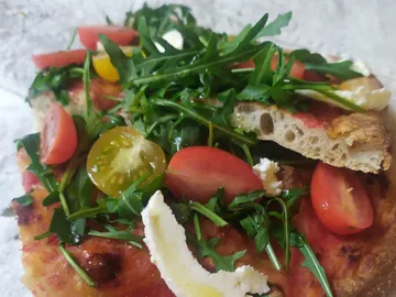 Pizza with tomatoes, arugula and white cheese on a table.