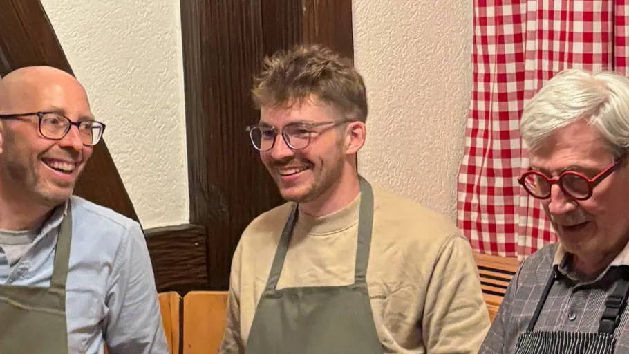 Drei Männer in Schürzen lächeln drinnen.