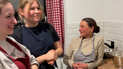 Three smiling women with aprons in kitchen.