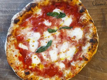 Pizza is on a wooden board, topped with tomatoes and cheese.