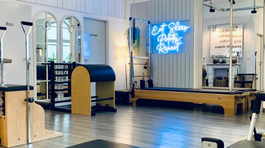 Pilates-Studio mit Neonschild, Geräte sichtbar.