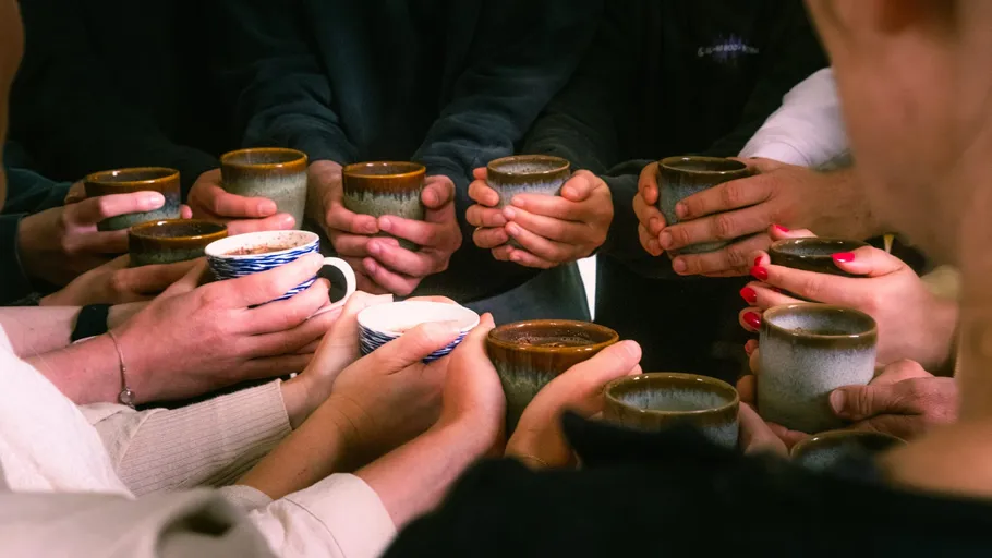 People holding mugs in a circle gathering.