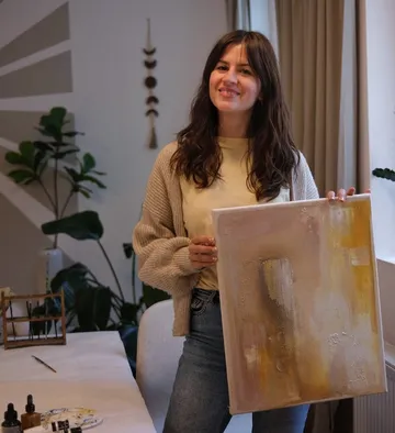 Woman holding canvas in art-filled room.