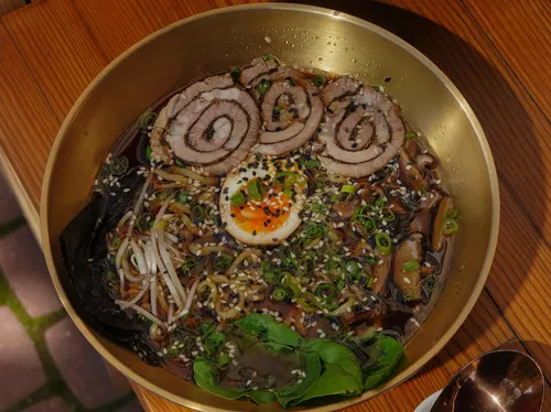 Ramen bowl with egg and pork slices outdoors.